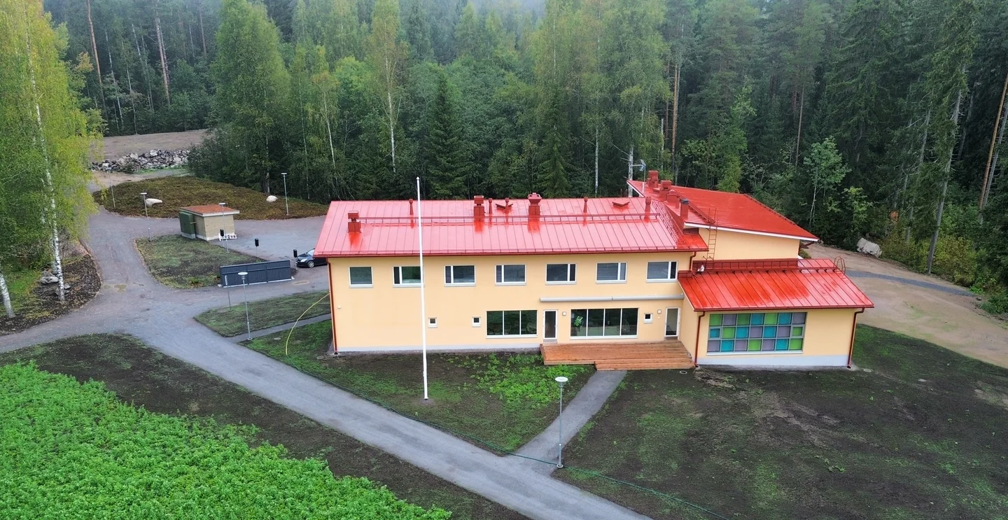 The pale facade, red metal roof and woodland surroundings of the accommodation and conference centre in Heinola